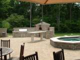 A landscape designer put a stonework outdoor kithen with pizza oven next to a spa shown in the background of this brick patio.
